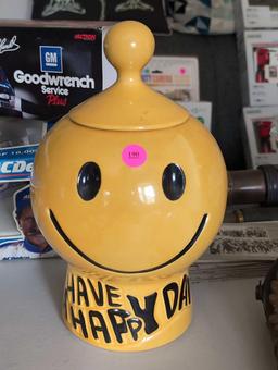 (LR) VINTAGE MCCOY POTTERY "HAVE A HAPPY DAY" SMILING FACE COOKIE JAR. SMALL CHIP ON LID. 11" TALL.
